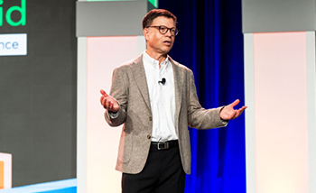A man wearing a suit and tie stands on stage, poised to deliver a presentation to the crowd